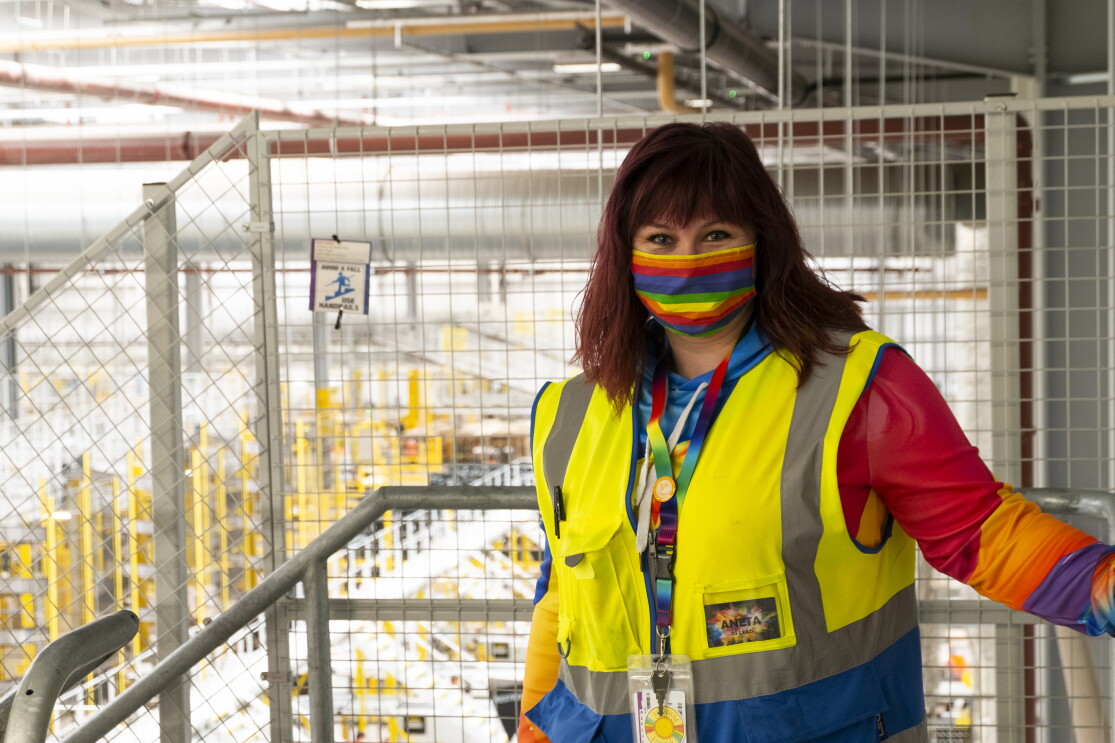 Amazon FC Lead Aneta Bachledova-Pateman wearing a yellow vest and a rainbow face mask, inside an Amazon site