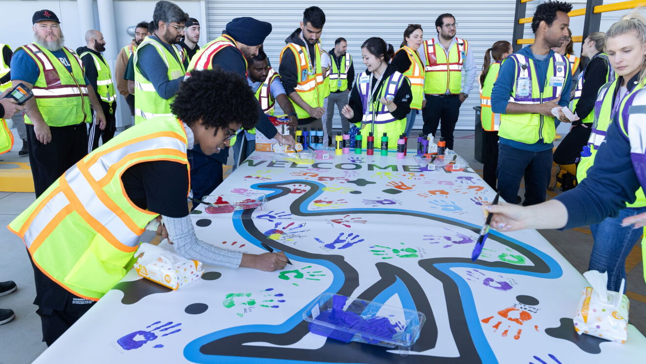 employees are drawing on a piece of banner for the opening of western sydney's amazon fulfillment centre