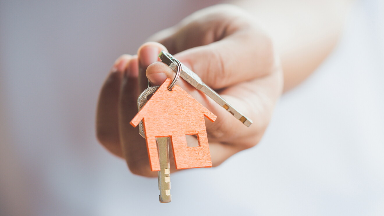 A woman's hand holding a set of keys with a keychain that shows a house on it. 