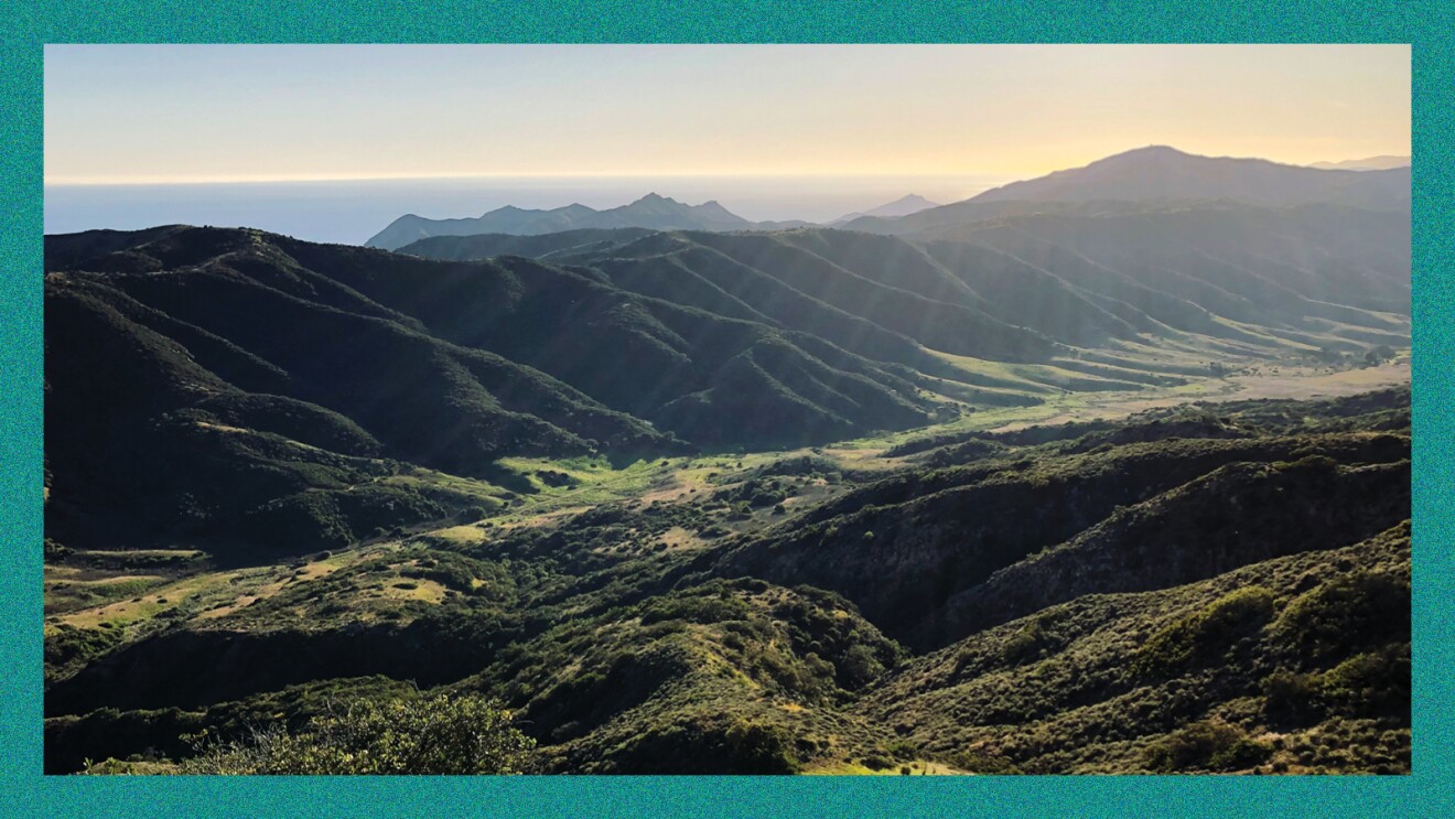 A photo of a mountain valley with the Pacific Ocean in the background of Santa Cruz Island. 