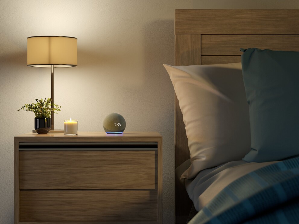 An Amazon Echo Dot on a nightstand next to a candle, a plant and a lamp.