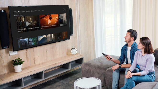 一对夫妻坐在沙发上看电视。这名男子将遥控器对准电视,调到《指环王:权力之戒》(The Lord of The Rings of Power)的x光片。