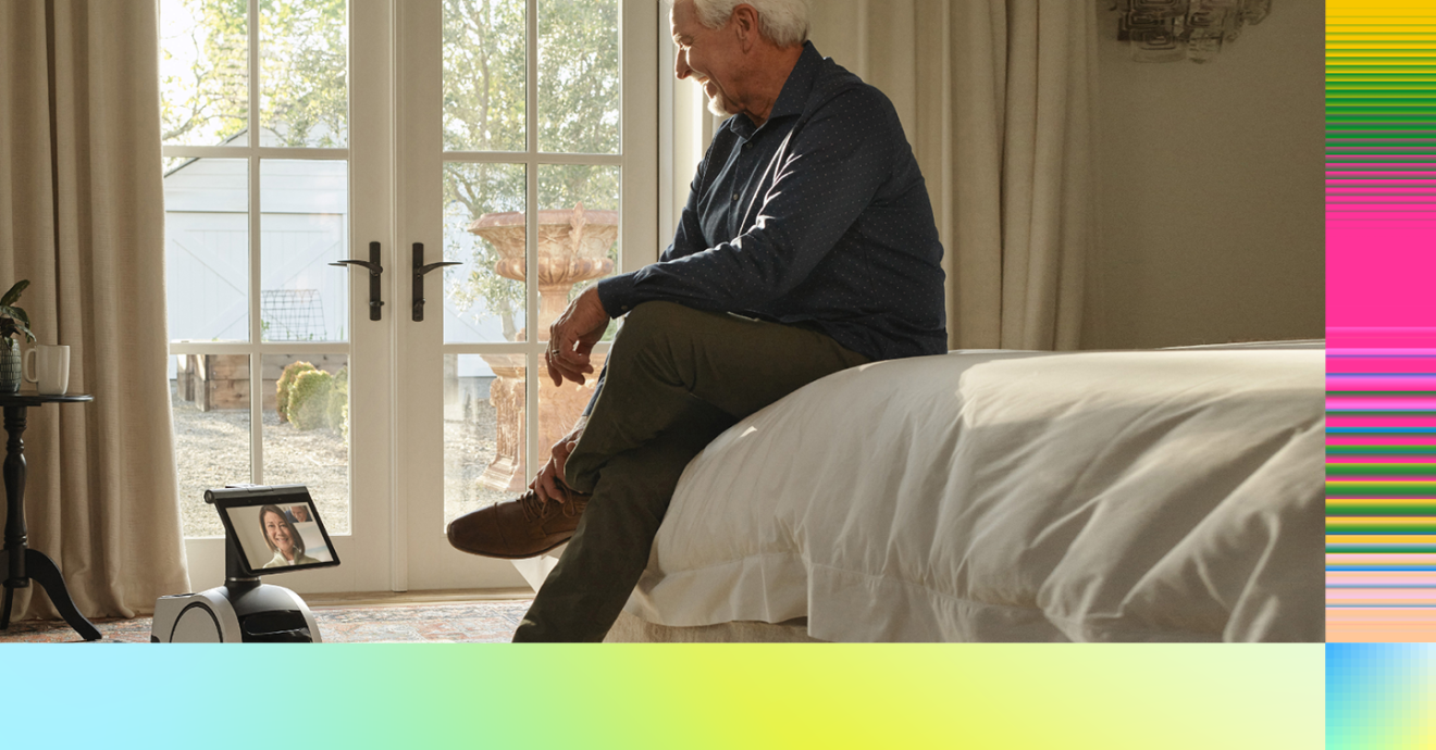 A man sitting on a bed, talking to an Astro robot in front of him.