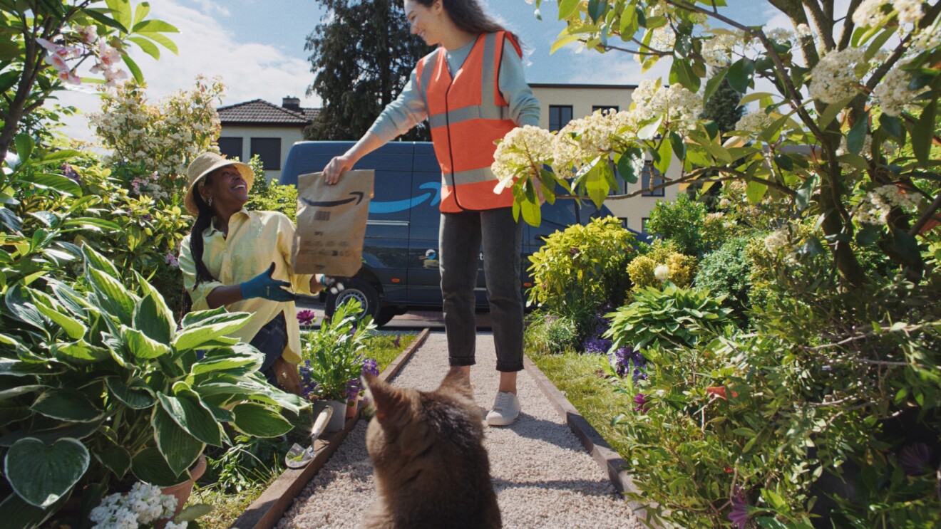 Le client reçoit son colis Amazon au milieu des fleurs épanouies et de la verdure.