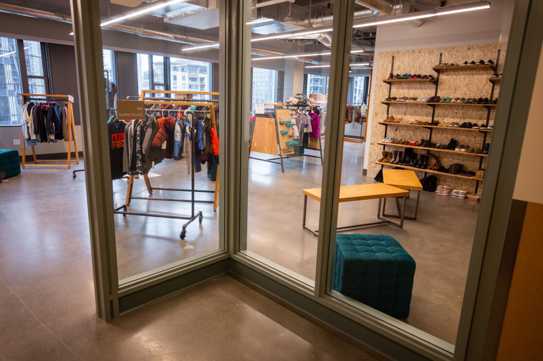 An image looking through a glass wall into a room with clothing on racks and shoes on shelves in a retail store-like setting.