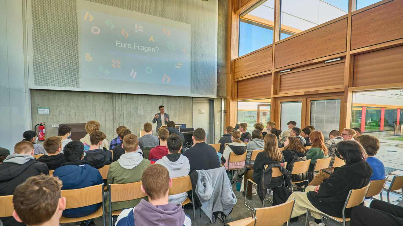 Deutschlandchef Rocco Bräuniger beim Amazon ClassChat vor einer Gruppe interessierter Schüler:innen, während im Hintergrund eine Präsentation gezeigt wird.