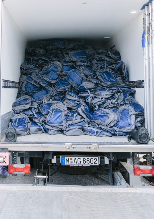 Die Klappe eines LKW ist geöffnet. Auf der Ladefläche sind Rucksäcke zu sehen, die sich bis an die Decke des LKW stapeln.