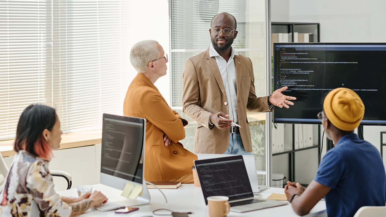 A photo of four employees meeting in a conference room. Language model coding is displayed on their devices.