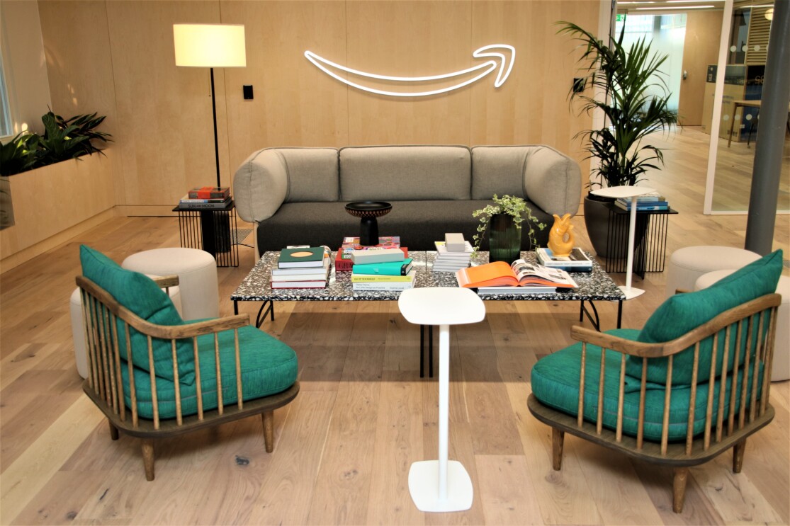 Cosy workspace featuring a gray sofa, teal chairs, and a neon Amazon smile