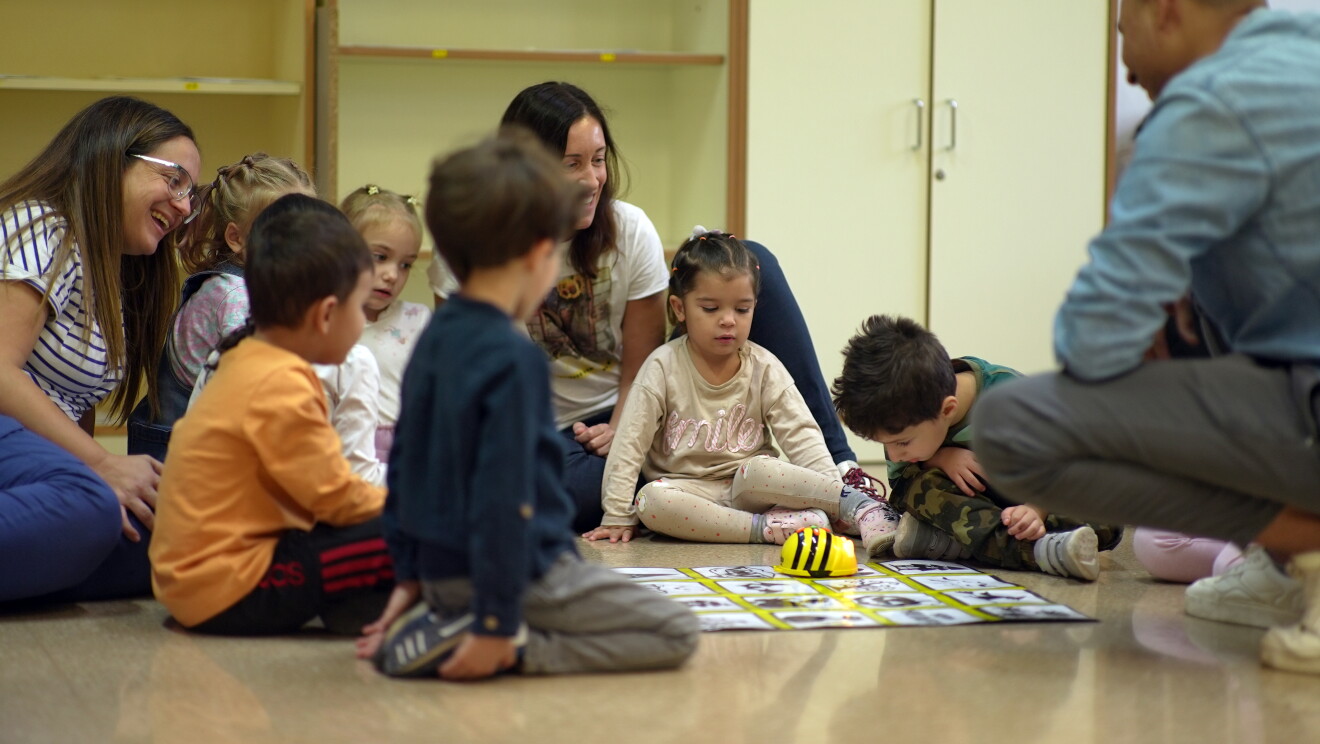 Aula de un colegio infantil con niños en el suelo mirando un robot durante la formación. 