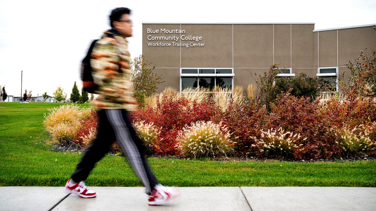 A photo of a student walking outside in front of a Blue Mountain Community College building.