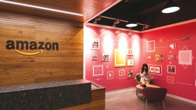 woman sitting in a chair reading from her phone. she is sitting inside an amazon office with red walls that contain artwork and graphics.