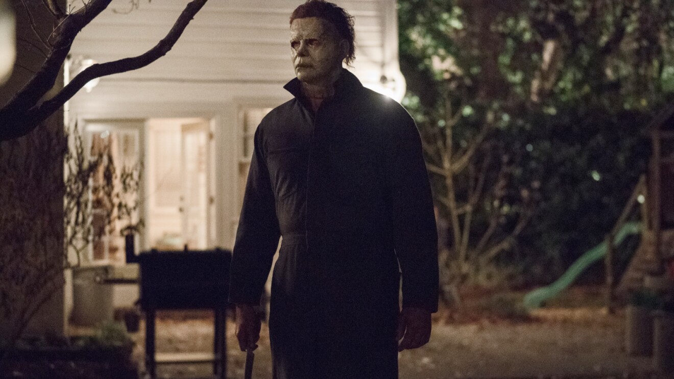 Menacing figure in dark clothing standing in shadowy yard at night