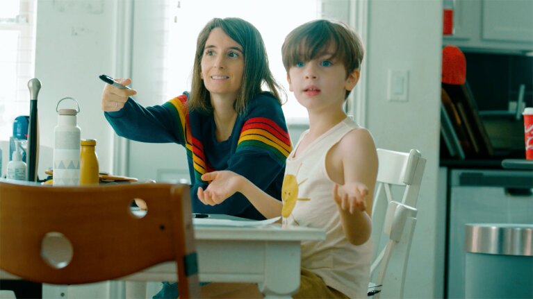 An image of a mom and her child looking across the room while sitting on the kitchen counter. The mom is pointing at something with a marker in her hand.