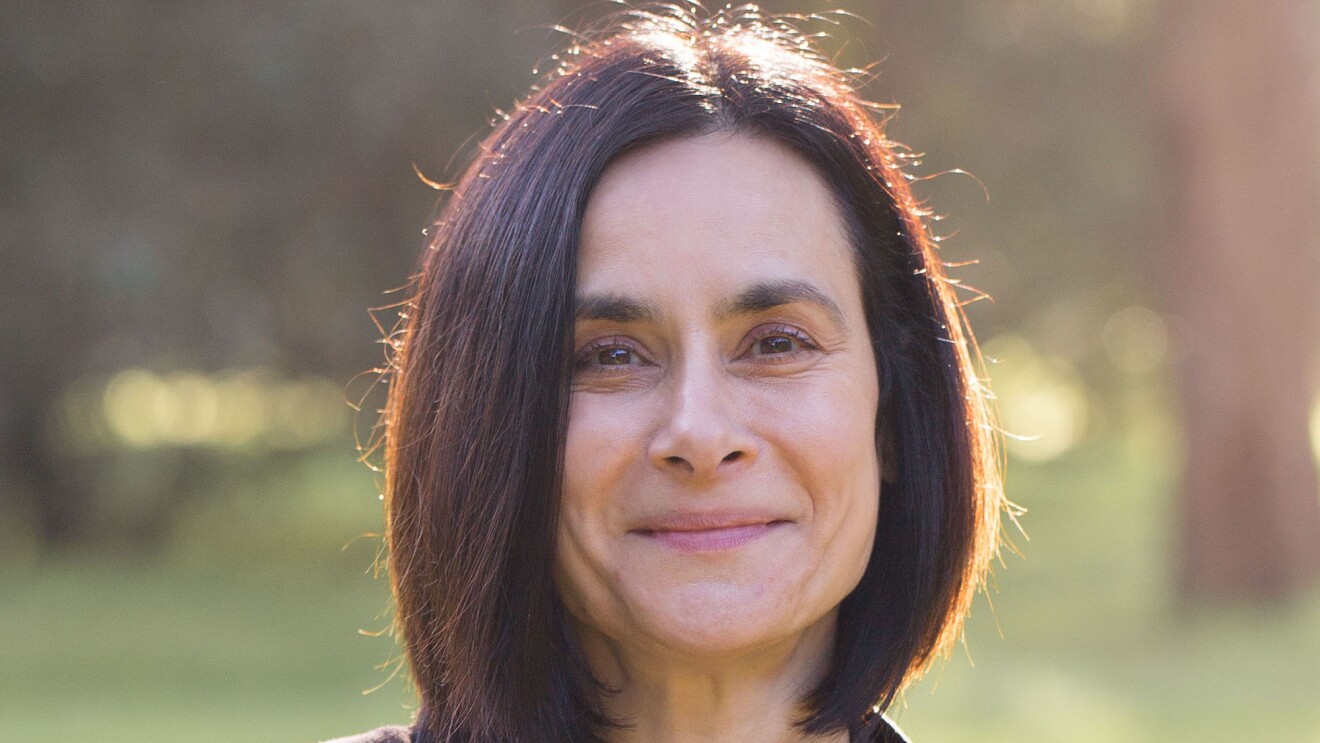 An image of Rose smiling for a photo outside in an area with green grass and trees in the background.