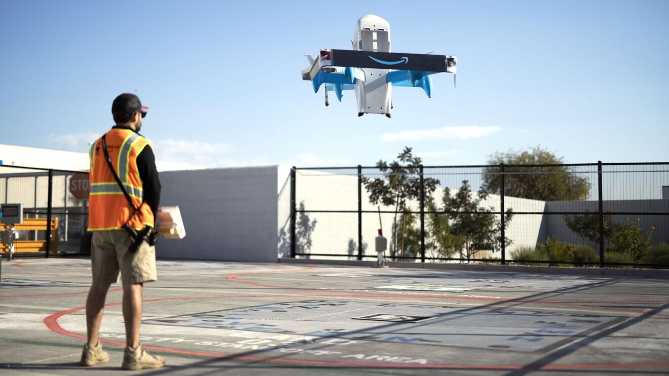 Aerial view of Prime Air drone taking off with safety-vested observer below.