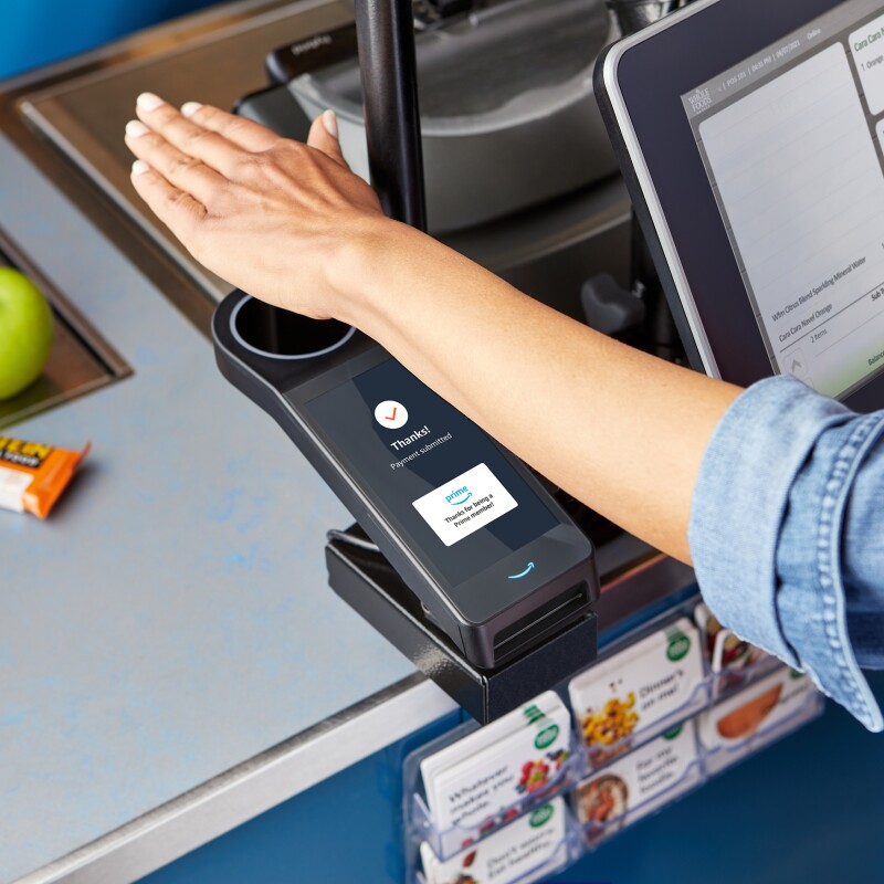 A hand hovers over a scanner at a grocery store, allowing a woman to check out and purchase her items.