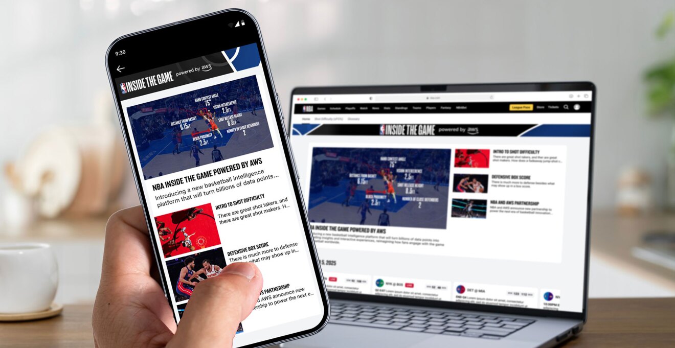 ぼやけたリビングの背景に、開いたノートパソコンと手前にスマートフォンを持つ左手。ノートパソコンにもスマートフォンにもバスケットボールの試合をデータ分析するサイトが表示されている。