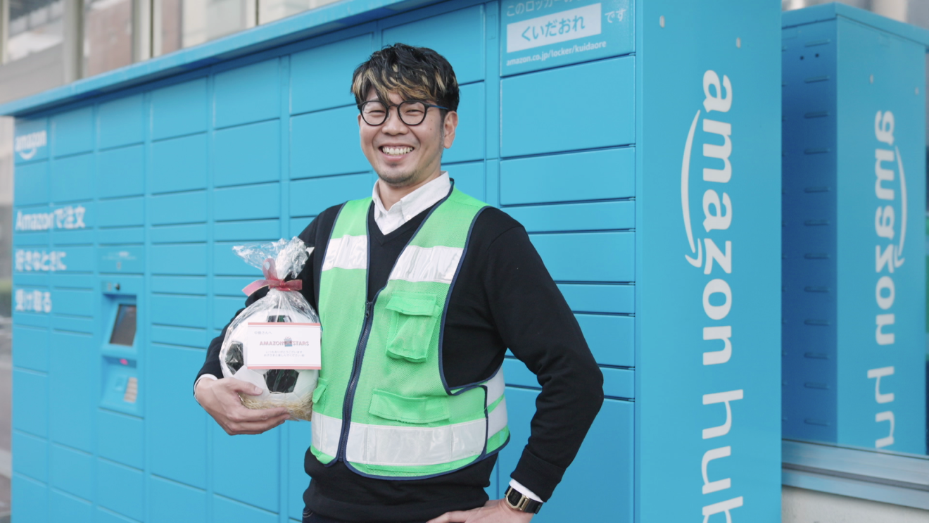 水色のAmazonロッカーの前に立つ笑顔のAmazon Flexドライバーの中島薫さん