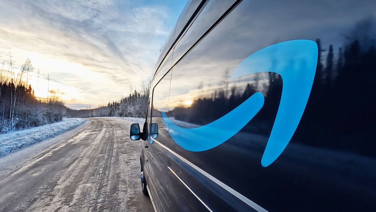 Amazon delivery vehicle driving on snowy road at sunset.