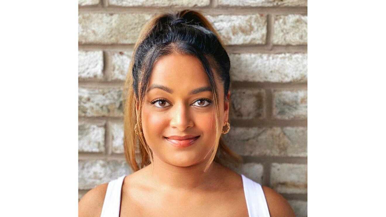 A headshot image of Krishni Rajah smiling for the photo standing in front of a brick wall.