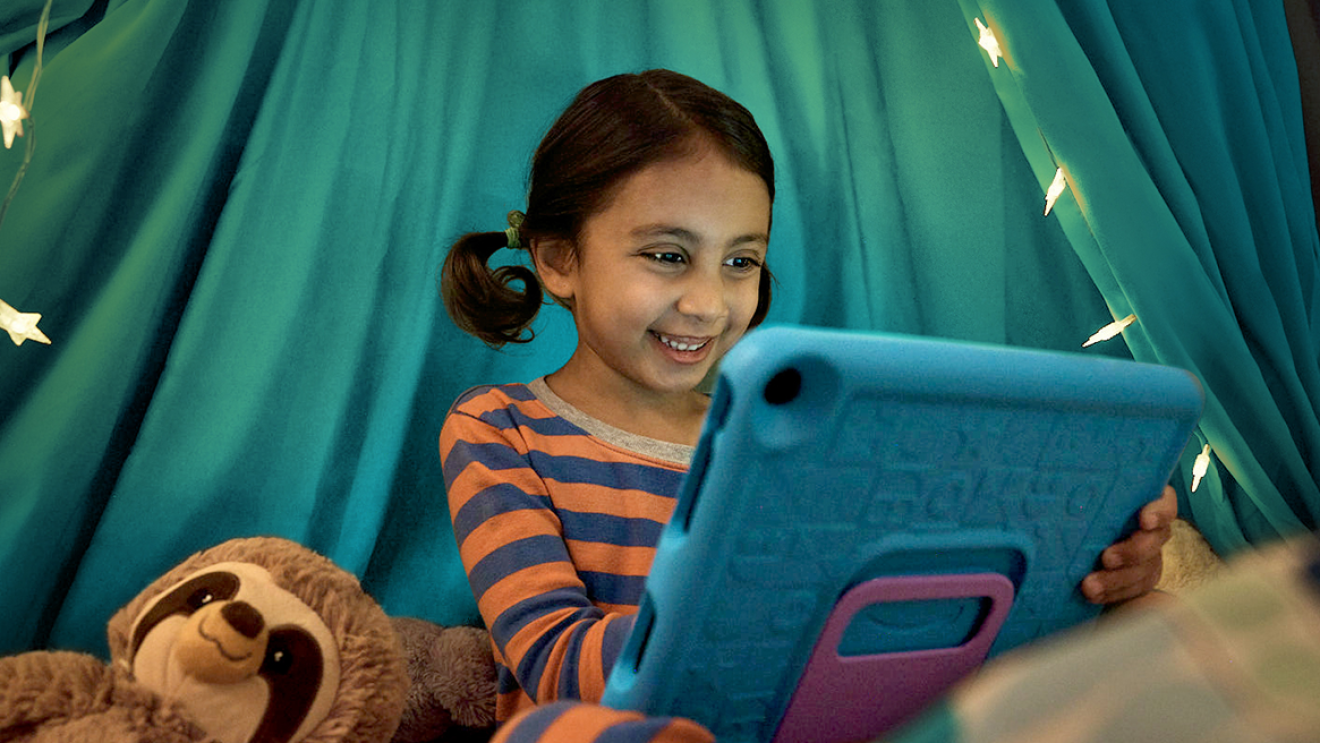 Smiling young girl using kindle device with a sloth stuffed animal on her right