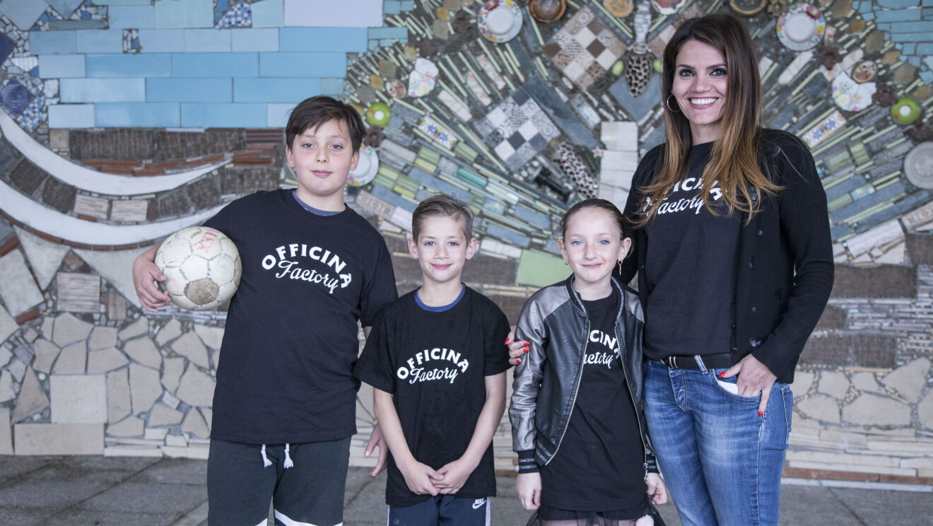 Alexandra Corona insieme a tre bambini sorridenti davanti a un murales della Biblioteca di Scampia