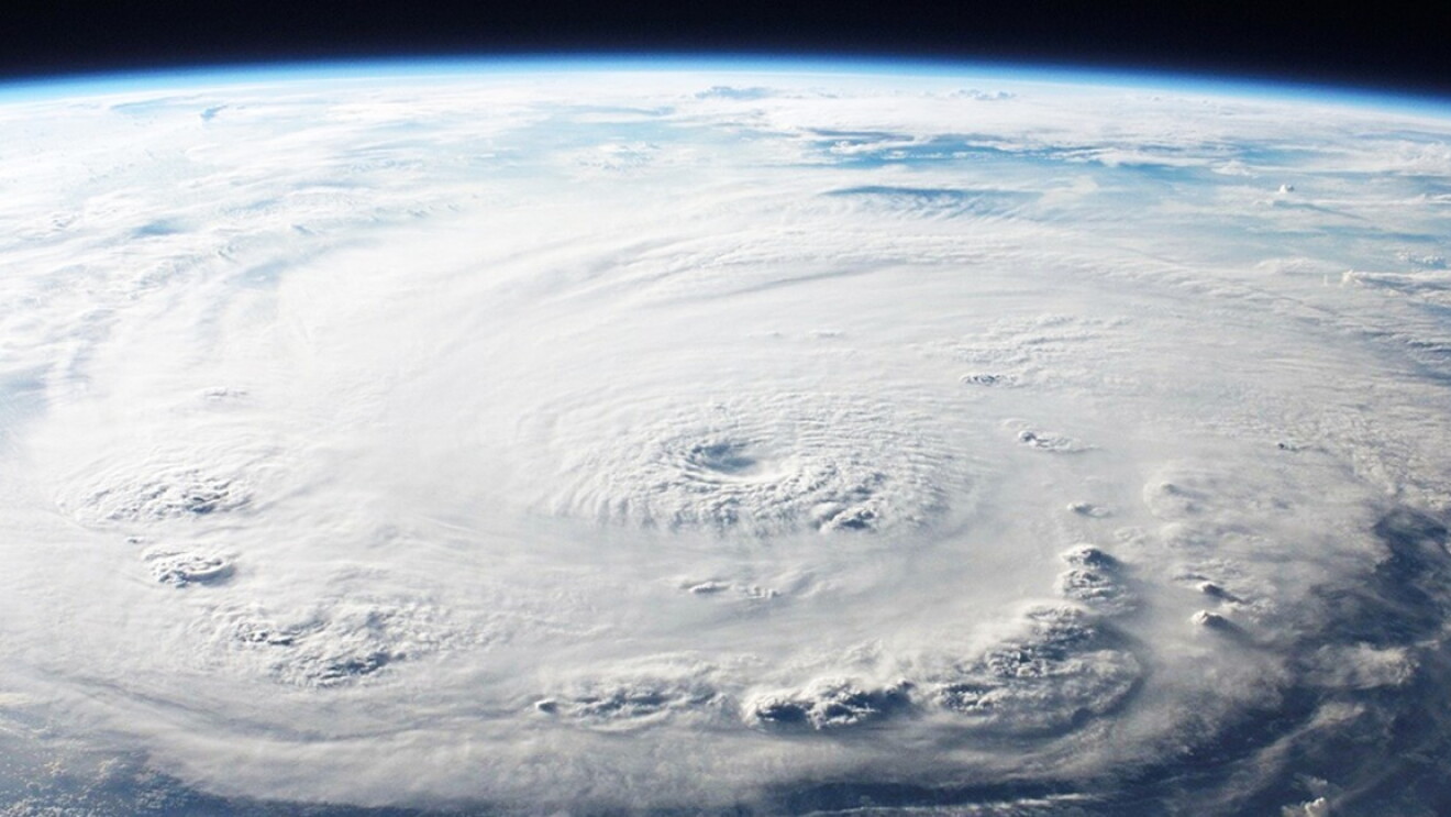 Foto de la tierra desde el espacio. Se ven nubes de color blanco y azul. También se ve una parte de cielo oscuro. 