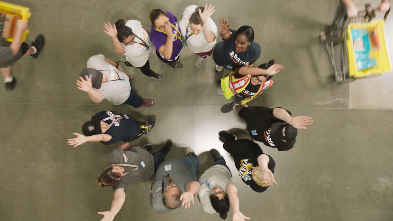 Overhead shot of people standing in a circle. They each have one hand raised.