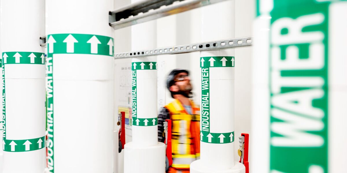 Worker in safety vest amid industrial water pipe labels