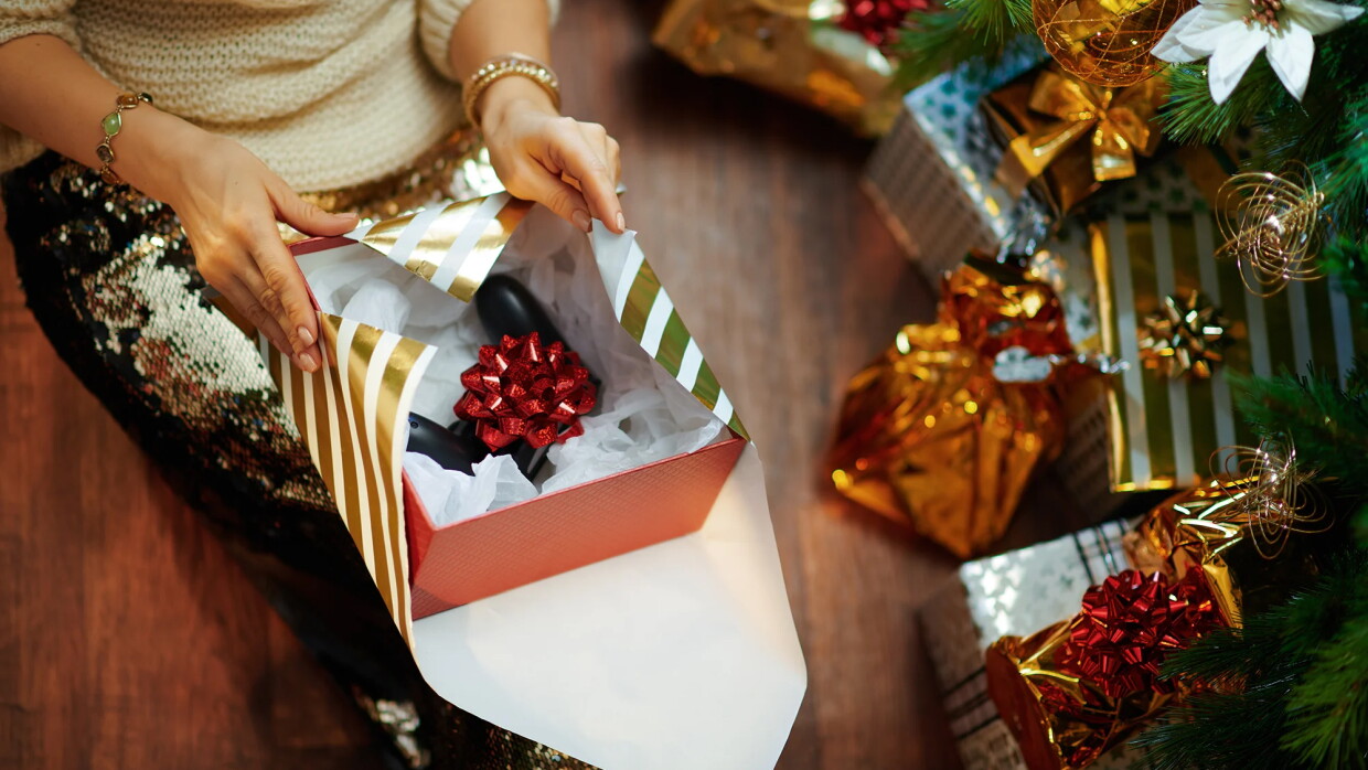 Primer plano de las mano de una mujer abriendo un paquete regalo con un mando de videojuegos sin su caja original. 