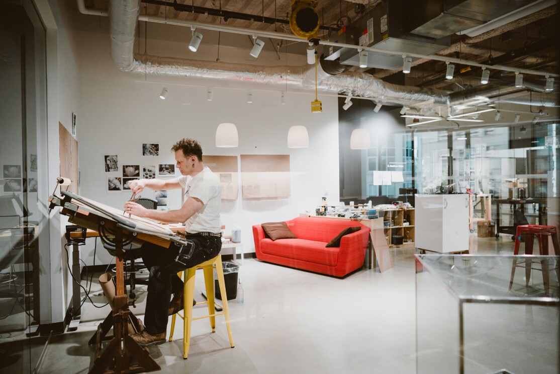 An artist sits at a raised desk, working on a project within an Amazon office building