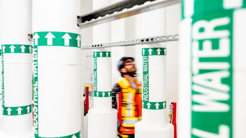Worker in safety vest amid industrial water pipe labels

