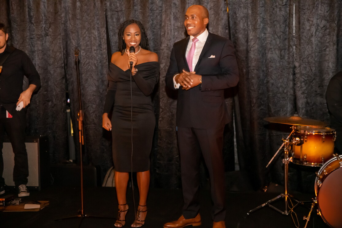 A man and a woman stand on a stage in formal wear in front of a microphone. 