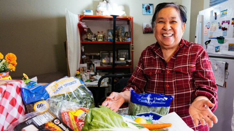 Smiling woman in plaid shirt with groceries and produce on table