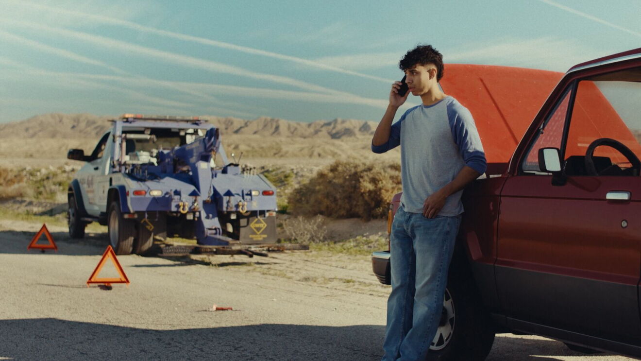 Person calling for roadside assistance while standing beside red vehicle in arid landscape
