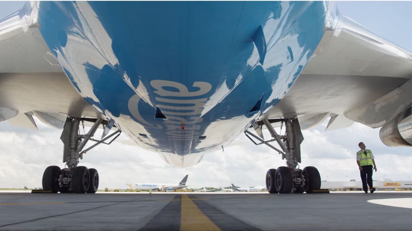 Ein Mitarbeiter läuft unter dem Flügel eines Amazon Prime Fliegers auf der Startbahn.