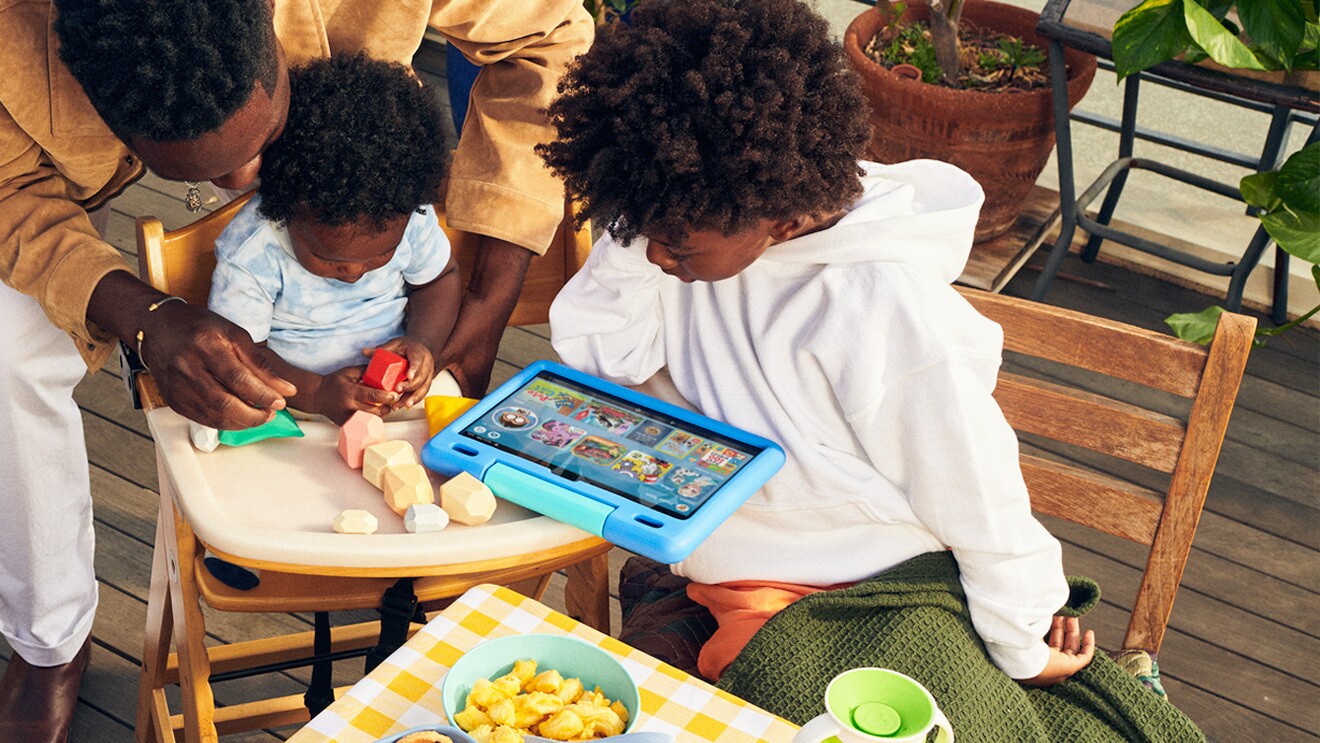 Family sits on deck while viewing Fire tablet.