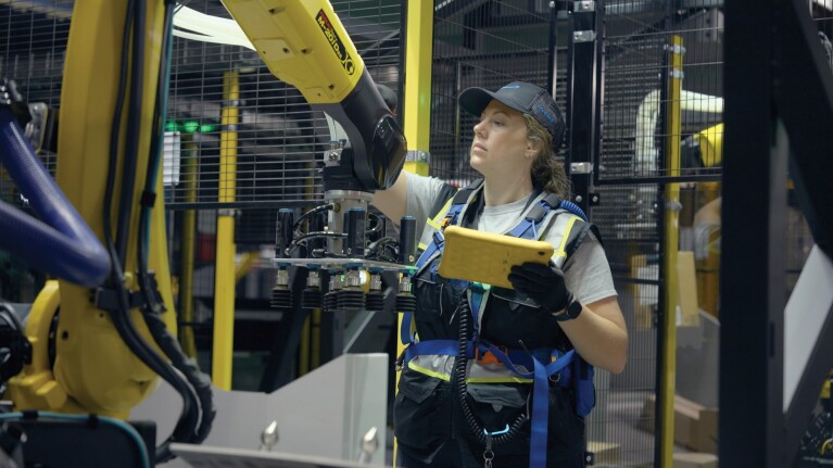 An Amazon employee wears safety gear and works with a robot in a fulfillment center.