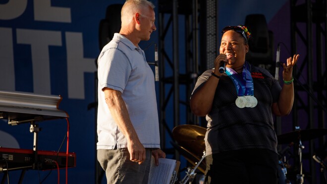 在舞台上,ESPN的肯尼·梅恩似乎准备采取麦克风说美国奥运期间闭幕式。旁边,特殊奥运选手阿里雷迪克是梅恩和观众来说,虽然穿着特殊奥运会的奖牌。