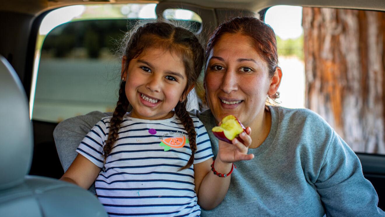 An image of a woman and a young girl smiling for a photo while sitting in a car.