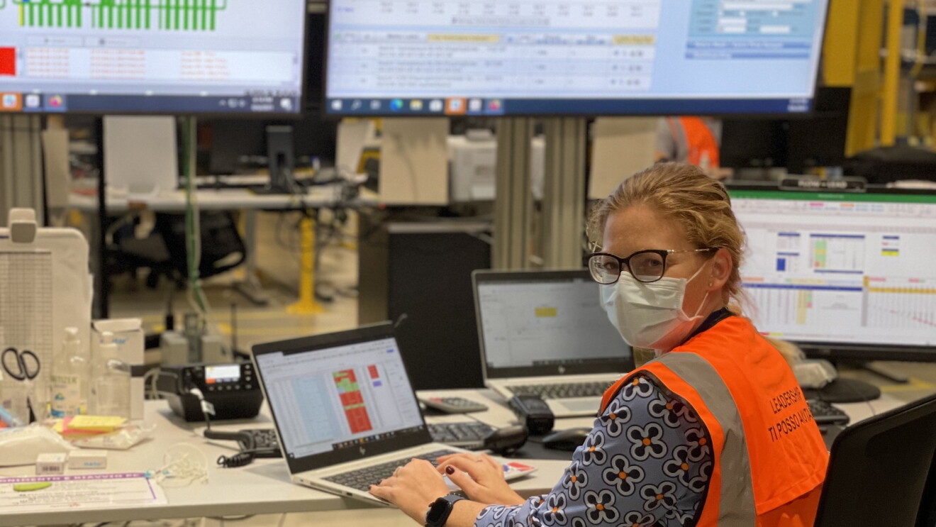 Donna seduta davanti ad un PC in un centro operativo Amazon. Indossa una mascherina chirurgica, ha i capelli biondi legati.