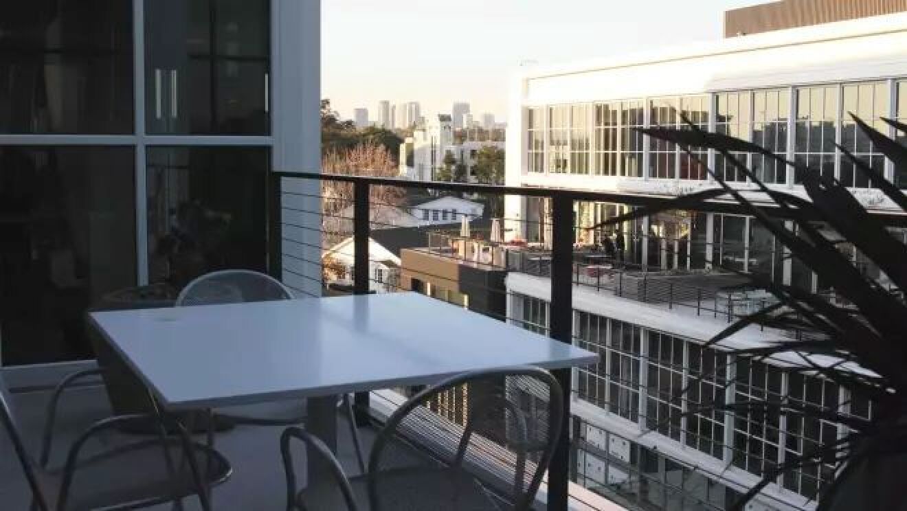 3つの椅子と白いテーブルが屋外のバルコニーに置かれている。