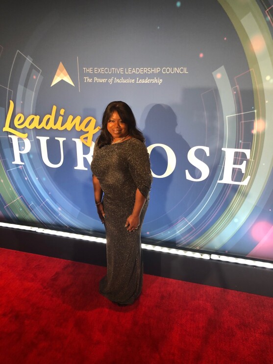 Nancy Dalton smiles for a photo on a red carpet in a long, sparkling gown in front of a backdrop that says "Leading Purpose."