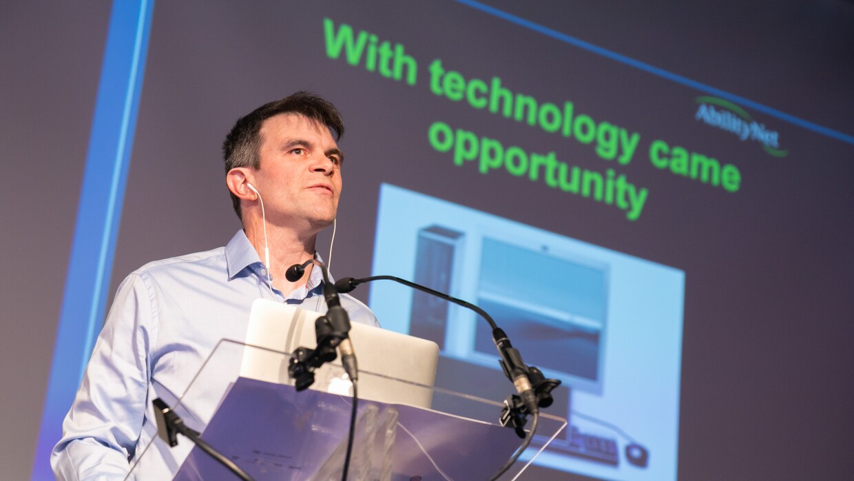 A close up image of Robin Christopherson standing at a glass podium giving a presentation.