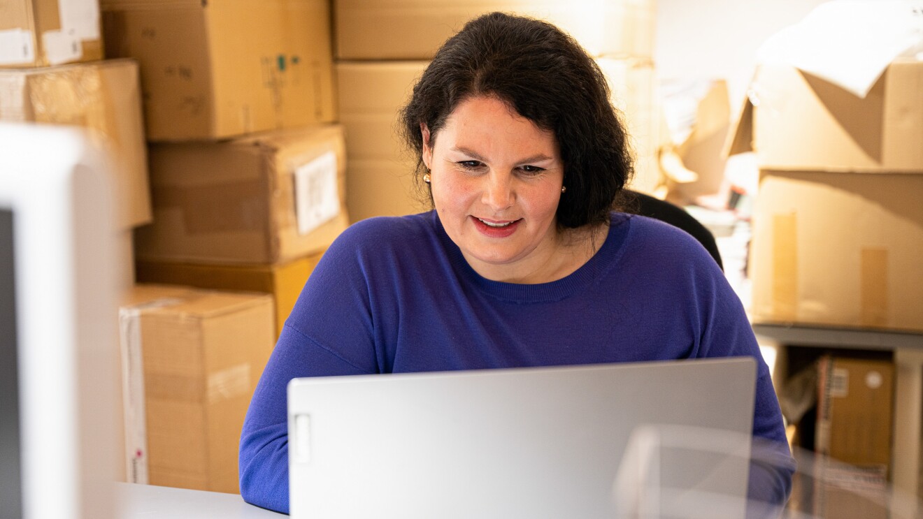 Eine Frau in einem blauen Pullover schaut in einen grauen Laptop.