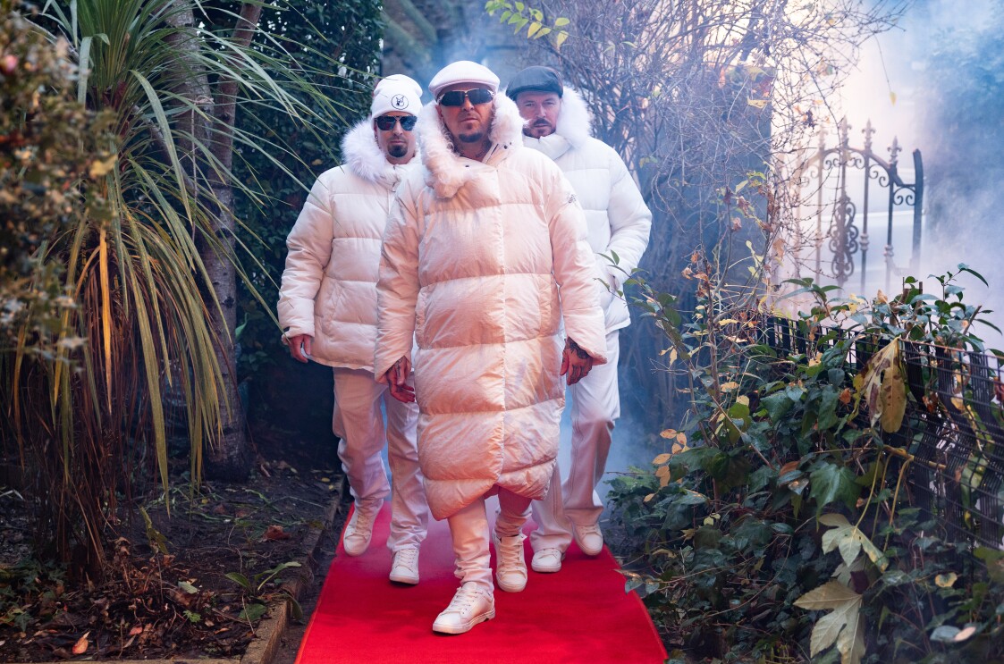 East 17 band members walk down a red carpet to someone's doorstep.