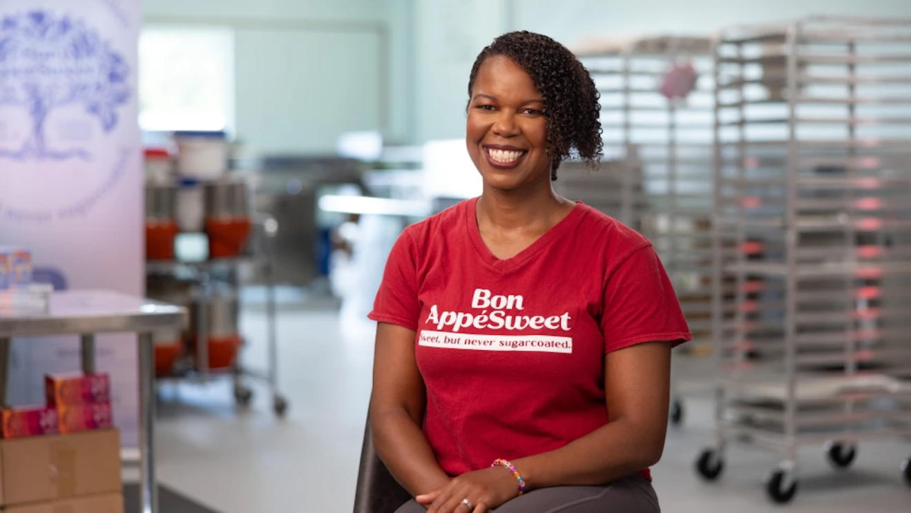 Thereasa Black, founder of Bon AppéSweet, sitting in her bakery in Leonardtown, Maryland, surrounded by rolling racks.