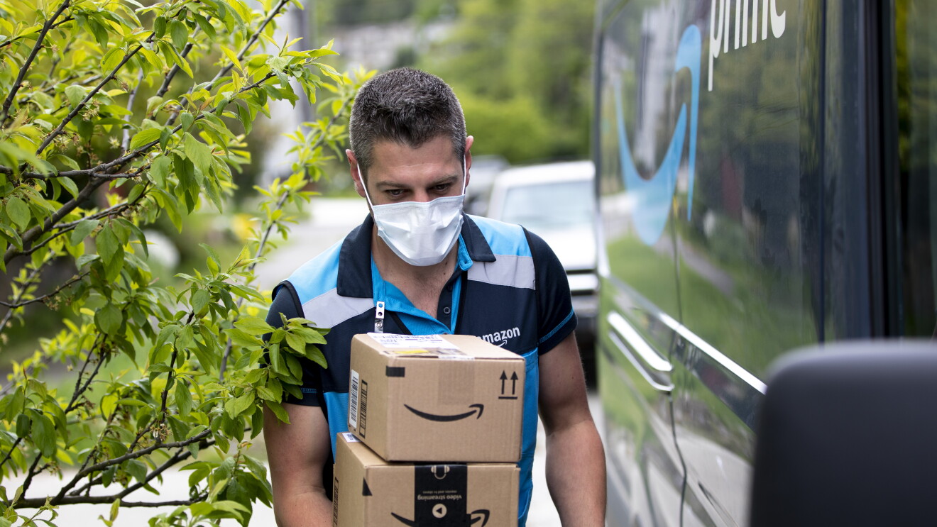Man wearing Amazon’s delivery driver uniform carries boxes, after exiting an Amazon Prime van.