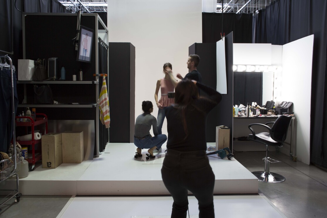 Two assistants, one male and one female, assist a model during an Amazon Fashion shoot. The photographer, who is silhouetted, is in the foreground.